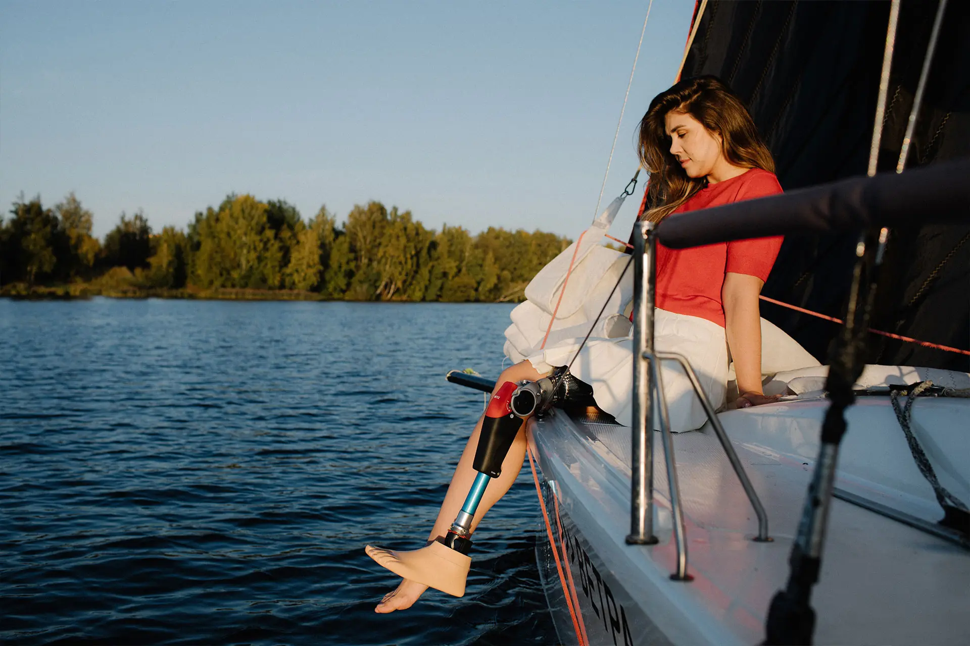Mulher sentada na borda de um barco no lago, com prótese de perna e pé de carbono