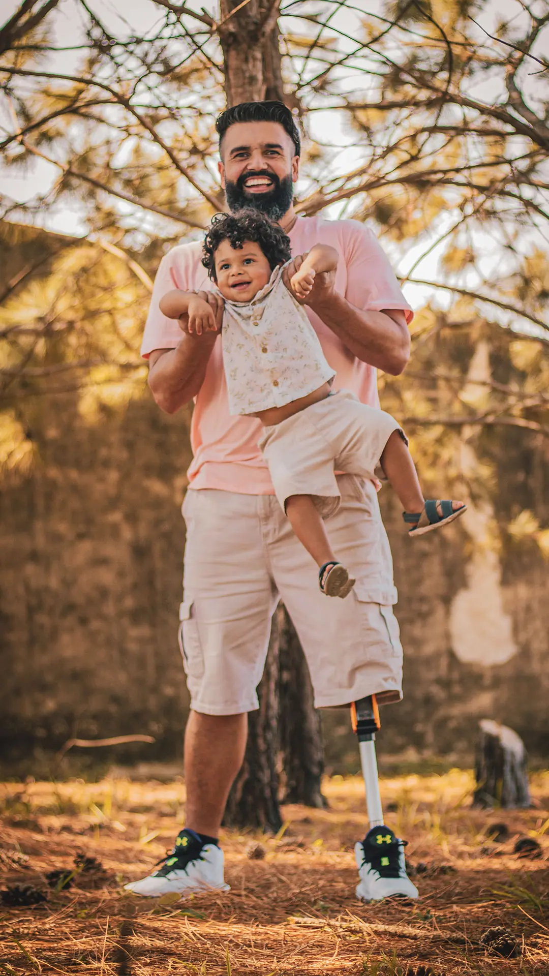 Pai com prótese de perna carregando o filho no colo num bosque